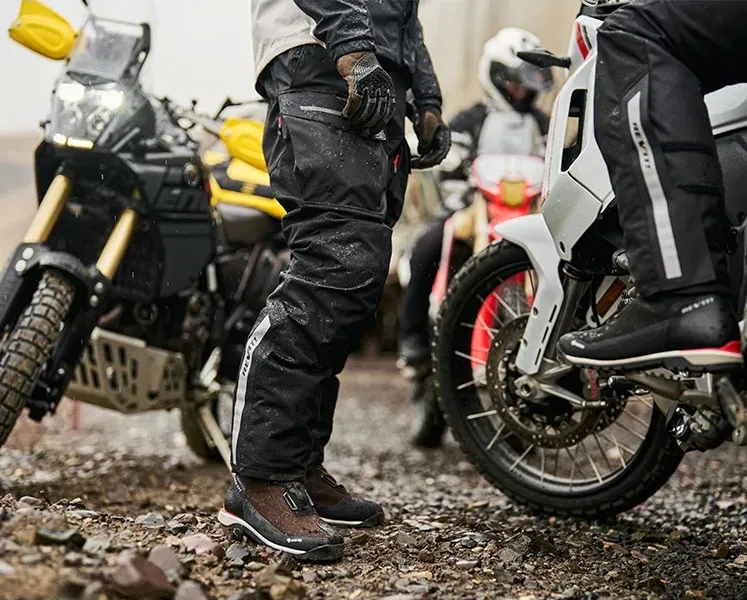 Detaliu outdoor pe REVIT Offtrack 2 H2O, cu motocicletă în fundal, util pentru discuția despre protecții integrate la genunchi